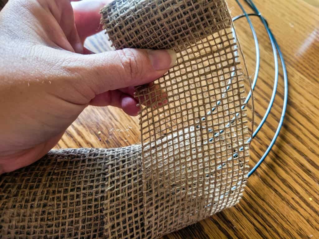 Photo of burlap ribbon being wrapped around a wire frame to make a wreath.